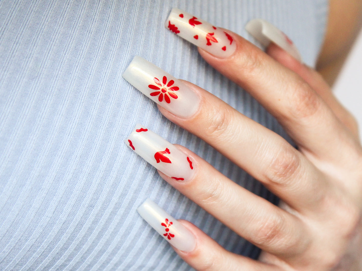 This image displays a set of red Talavera nail stickers showcasing various designs. The ring finger features two small birds with decorative accents. The middle finger showcases a single daisy design. The index finger depicts a single bird surrounded by decorative corner pieces. The pinky and thumb nails each display traditional Talavera decorative patterns.