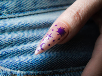 A celestial landscape graces the thumb: a vibrant sun, a twinkling star, a crescent moon, dots and sparkles complete the starry scene.